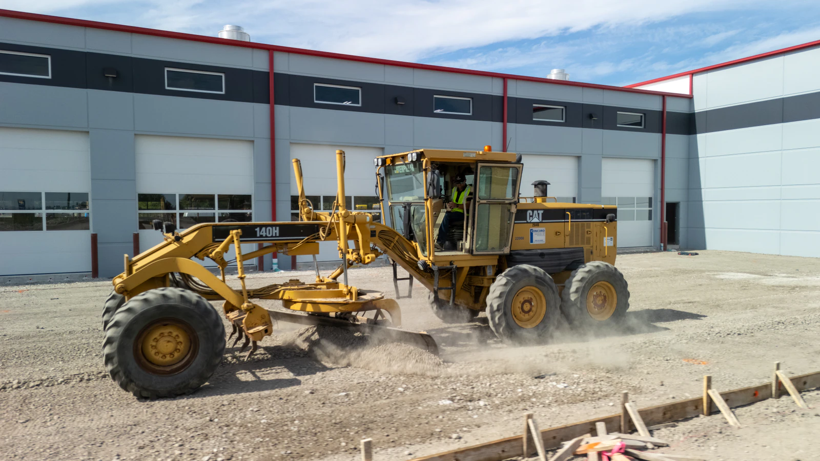 Motor grader fine-grading aggregate base in front of a new commercial building during general site contracting